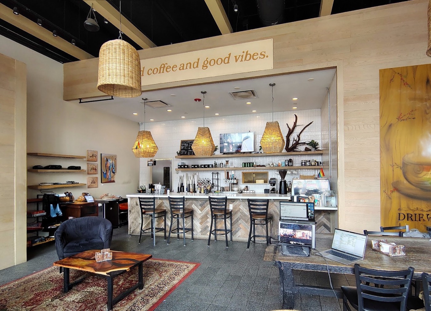 The coffee bar at Driftwood, with woven pendant lights, a herringbone wood counter, and a “good coffee and good vibes” sign above.