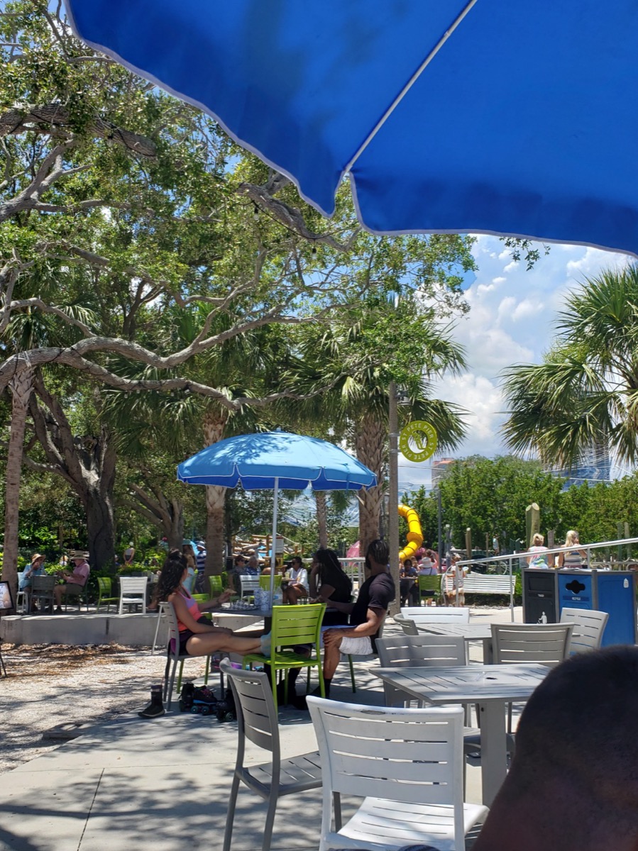 Shaded sidewalk patio seating under blue umbrellas near downtown St. Petersburg.