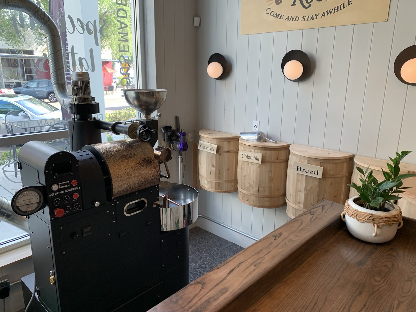 Driftwood’s drum coffee roaster beside wooden barrels labeled Guatemala, Colombia, and Brazil.